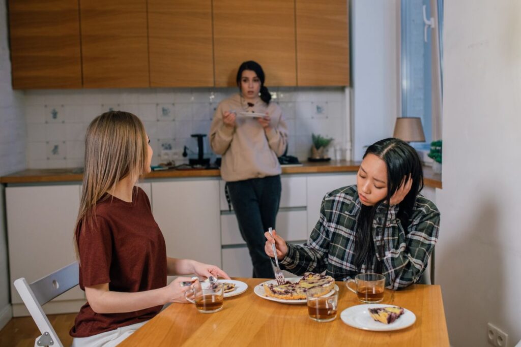 Three friends in a kitchen, one looking withdrawn while the others talk over tea and pie