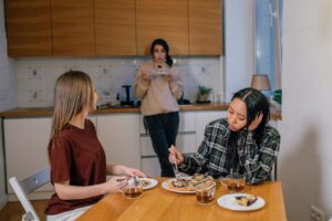 Three friends in a kitchen, one looking withdrawn while the others talk over tea and pie